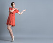 Full length image of young Asian woman wearing orange dress on gray background