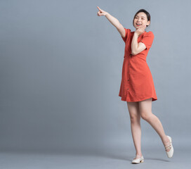 Wall Mural - Full length image of young Asian woman wearing orange dress on gray background