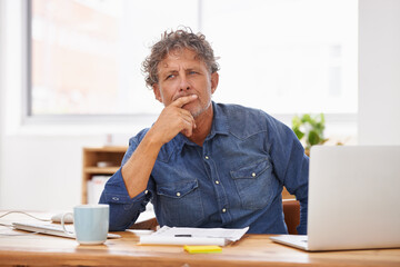 Thinking about business. Shot of a mature businessman sitting at his office desk and looking thoughtful.