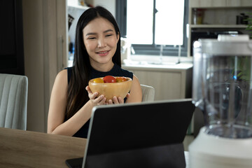 Wall Mural - Healthy asian woman enjoy making green vegetables smoothie and reading recipe on digital tablet.