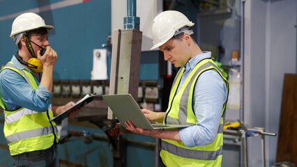 Two professional industrial engineer specialist with safety vast uniform and helmet holding laptop checking security of electrical control panel in private sector of industry safety security concept