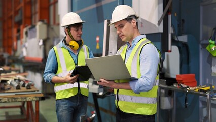 Two professional industrial engineer specialist with safety vast uniform and helmet holding laptop checking security of electrical control panel in private sector of industry safety security concept