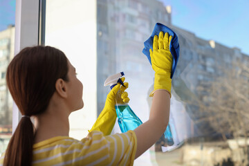 Canvas Print - Young woman cleaning window glass with rag and detergent at home, back view