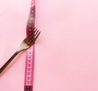Fork  with measuring tape around on a pink background .Weight loss concept