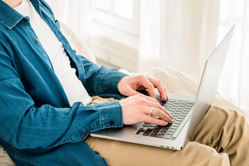 Canvas Print - hands a young man in a blue shirt using a laptop on his lap while sitting on the couch. cozy conditi