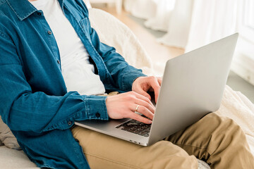 Canvas Print - hands a young man in a blue shirt using a laptop on his lap while sitting on the couch. cozy conditi