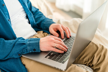 Canvas Print - hands a young man in a blue shirt using a laptop on his lap while sitting on the couch. cozy conditi