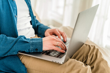 Canvas Print - hands a young man in a blue shirt using a laptop on his lap while sitting on the couch. cozy conditi