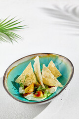 Appetizers with avocado, stracciatella and tortilla chips. Avocado starter with stracciatella cheese in ceramic dish. Menu for Keto diet. Modern food in white stone background