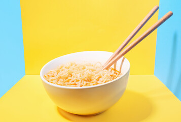 Wall Mural - A bowl with instant noodles and chopsticks on blue and yellow background.