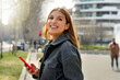 © zigres - Relaxed girl looking back holding mobile phone with blurred city background