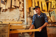 © bondvit - Senior carpenter in uniform works with a wood on a woodworking machine at the carpentry manufacturing