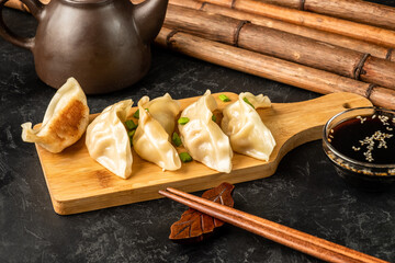 Sticker - Asian gyoza dumplings on a wooden board on a dark textured background. Next to the background is a teapot and bamboo.