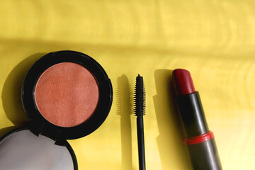 Lipstick, mascara and blush on bright yellow background. Flat lay.