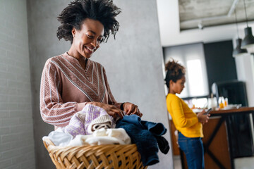 Wall Mural - Happy single black mother and child doing household chores, child using smartphone at home