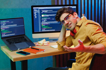 Side view young confused sad puzzled wondered software engineer IT specialist programmer man in shirt work at home writing code on laptop pc desktop computer spread hands. Program development concept