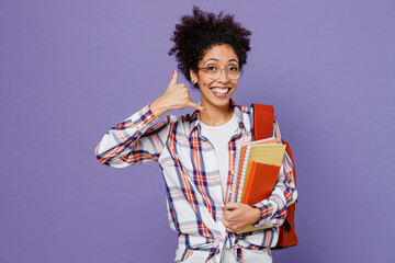 Wall Mural - Young girl woman of African American ethnicity teen student in shirt backpack doing phone gesture like say call me back isolated on plain purple background Education in high school university concept