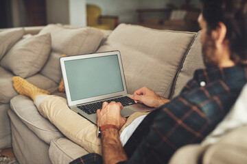 Canvas Print - This is how I keep up with the world. Shot of a handsome young man using his laptop while relaxing on a couch at home.