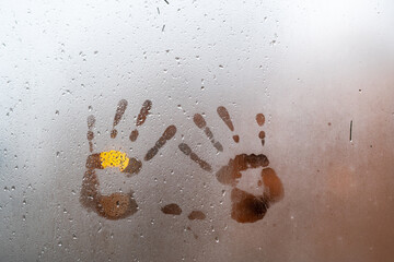 vidrio de ventana empañado por lluvia afuera con dos manos marcadas en el interior