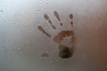 vidrio de ventana empañado por lluvia afuera con manos marcadas en el interior