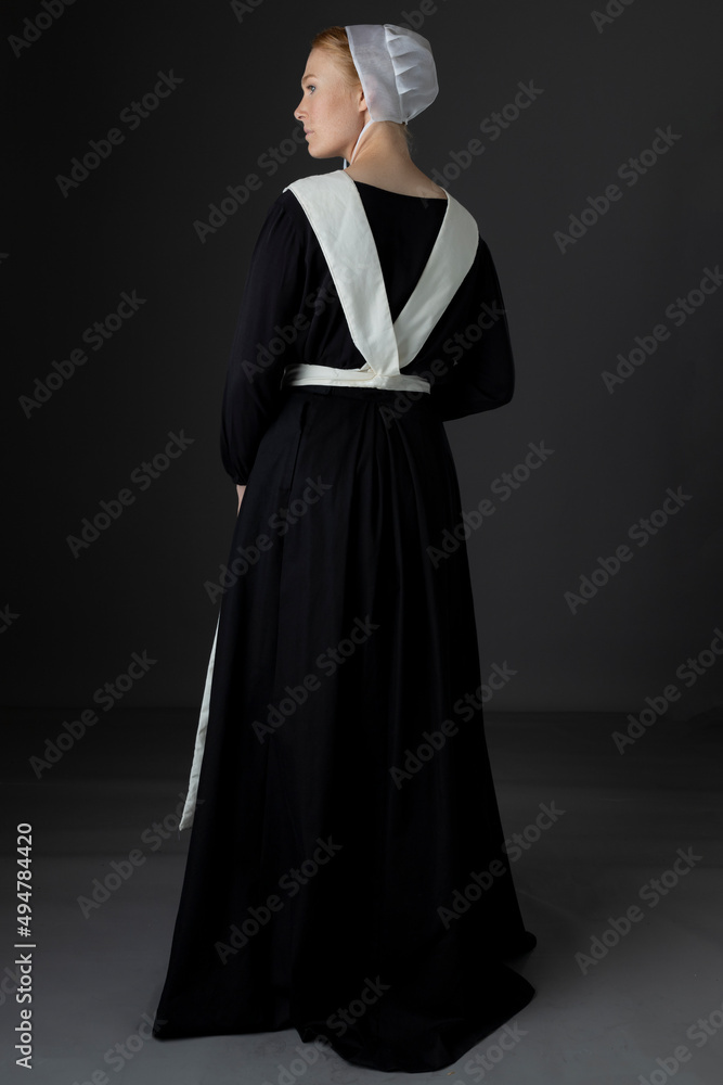 An Amish woman wearing a black dress with a white apron and cap standing  against a studio backdrop Stock-foto | Adobe Stock