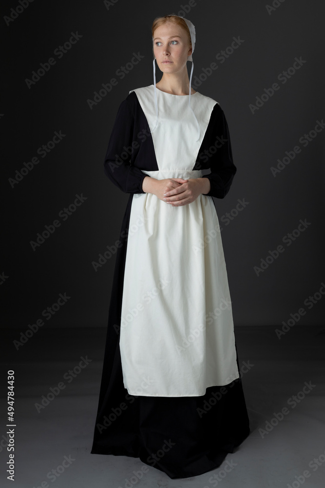 An Amish woman wearing a black dress with a white apron and cap standing against a studio backdrop Stock Photo | Adobe Stock An Amish woman wearing a black dress with a white apron and cap standing against a studio backdrop Stock Photo | Adobe Stock