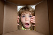 © Volodymyr - The surprised child unpacking, opening carton box and looking inside. The package, delivery, surprise, kids gift concept. Closeup kids face.