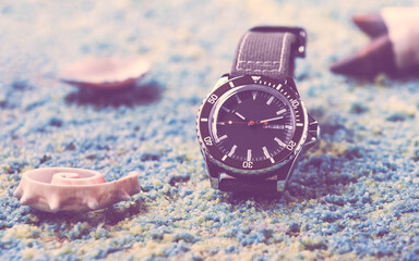 Diving watch of the famous Swiss brand Mido, which is on a background with blue sand, shells and starfish.