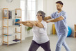 Home assistance, physiotherapy and healthy lifestyle for elderly. Professional rehabilitation doctor provides medical services to elderly woman at her home. Joyful retired woman doing stretching.