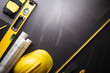 Business contraction theme. Tool kit of the contractor: yellow hardhat, libella, hand saw. Plans and notebook on the gray tiles.