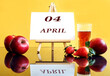 © MARYIA - Calendar for April 4: an easel with the inscription 04, april, apples and strawberries next to it, a glass of freshly squeezed juice, yellow background, side view