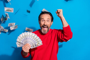 Sticker - Portrait of attractive cheerful man holding cash flying credit loan rejoicing isolated over bright blue color background