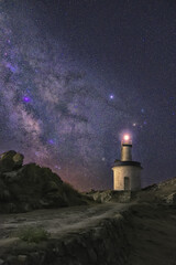 Poster - Vertical shot of an illuminated lighthouse placed on a shore in the background of a starry sky.