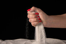 Female Hand Squeezing And Spilling Handful Of White Dry Sand On Black Studio Background. Sand Particles Sifting Through Fingers. Close Up Of Grains Of Pure Natural Mineral Quartz In Female Hand.