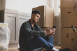 © ReeldealHD images - Mid adult male sitting on the floor in new home using smartphone surrounded by boxes