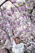 © Denys - A blonde woman in a white shirt poses near the cherry blossoms. Spring mood