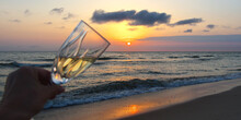A Glass Of Sparkling Wine In Hand.  Bright Beautiful Sunset At The Calm Sea. Solar Disk Over Water. Selective Focus.