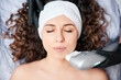 Top view of attractive young woman with closed eyes wearing white headband while receiving facial treatment at wellness center. Female patient having face lifting procedure in cosmetology clinic.