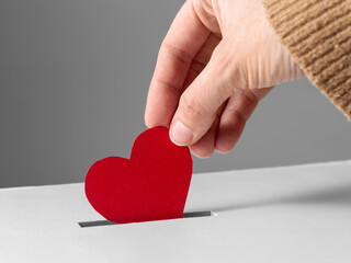 Wall Mural - charity, love and valentine's day concept - close up of hand putting red heart into donation box