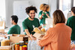 canvas print picture - charity, donation and volunteering concept - happy smiling male volunteer with clipboard and woman taking box of food at distribution or refugee assistance center