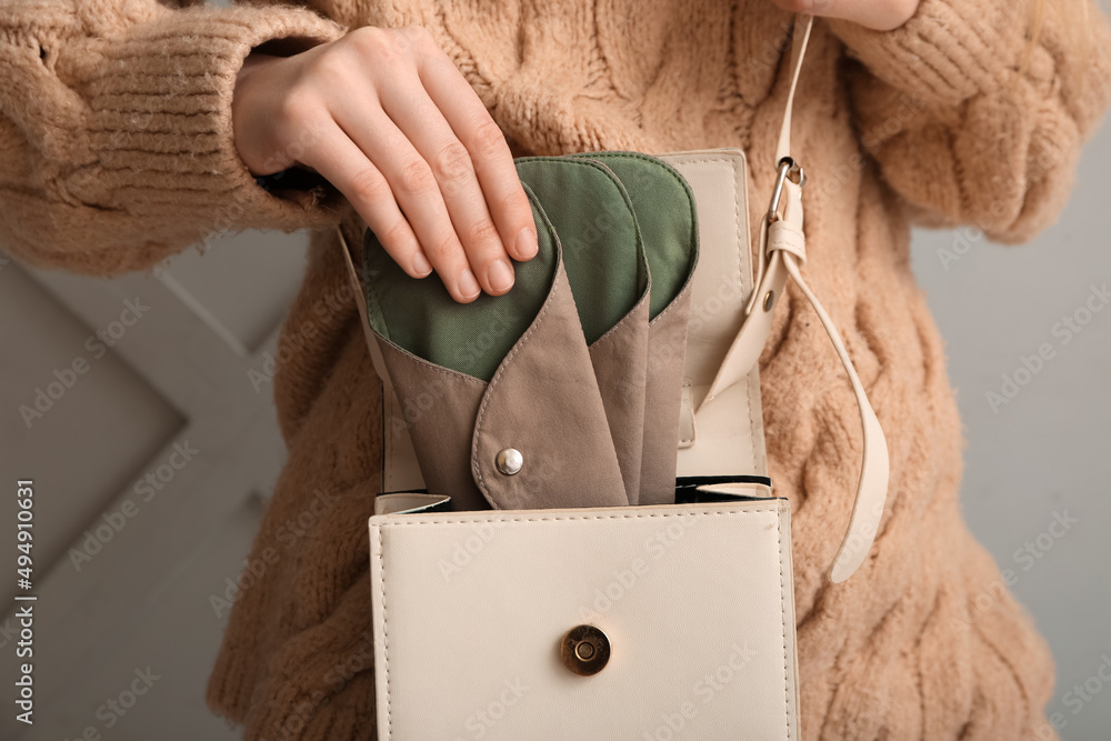 Woman putting reusable menstrual pads in bag on light background