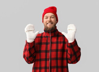 Wall Mural - Young bearded man in warm gloves and hat on light background