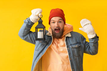 Wall Mural - Happy young bearded man in warm gloves with lantern on yellow background
