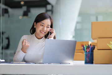 Wall Mural - Happy young Asian woman entrepreneur, Smile for sales success after checking order from online shopping store on laptop at home office. Concept online start up small business and e-commerce.