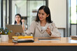 © saltdium - A portrait of a young pretty Asian businesswoman using a laptop while sitting at workspace and having a coffee, for business and technology concept.