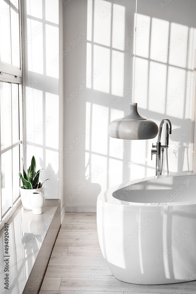 Modern bathtub and lamp near white wall in light room