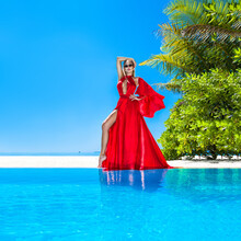 Luxury Fashion. Elegant Fashion Model. Stylish Female Model In Red Long Gown Dress On The Maldives Beach. Elegance. Classy Woman In Amazing Red Dress Near The Pool. Couture. Vogue.