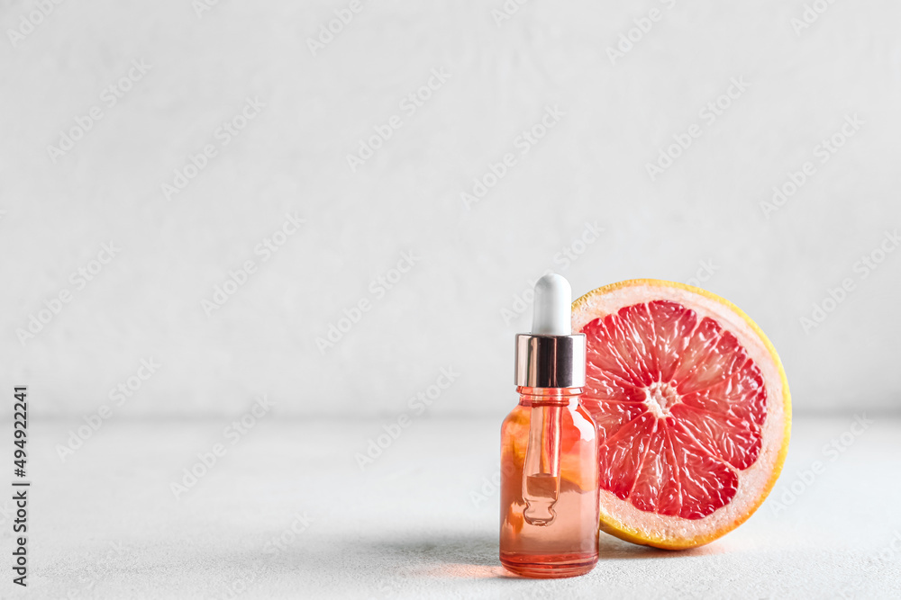 Bottle with essential oil and half of ripe grapefruit on light background