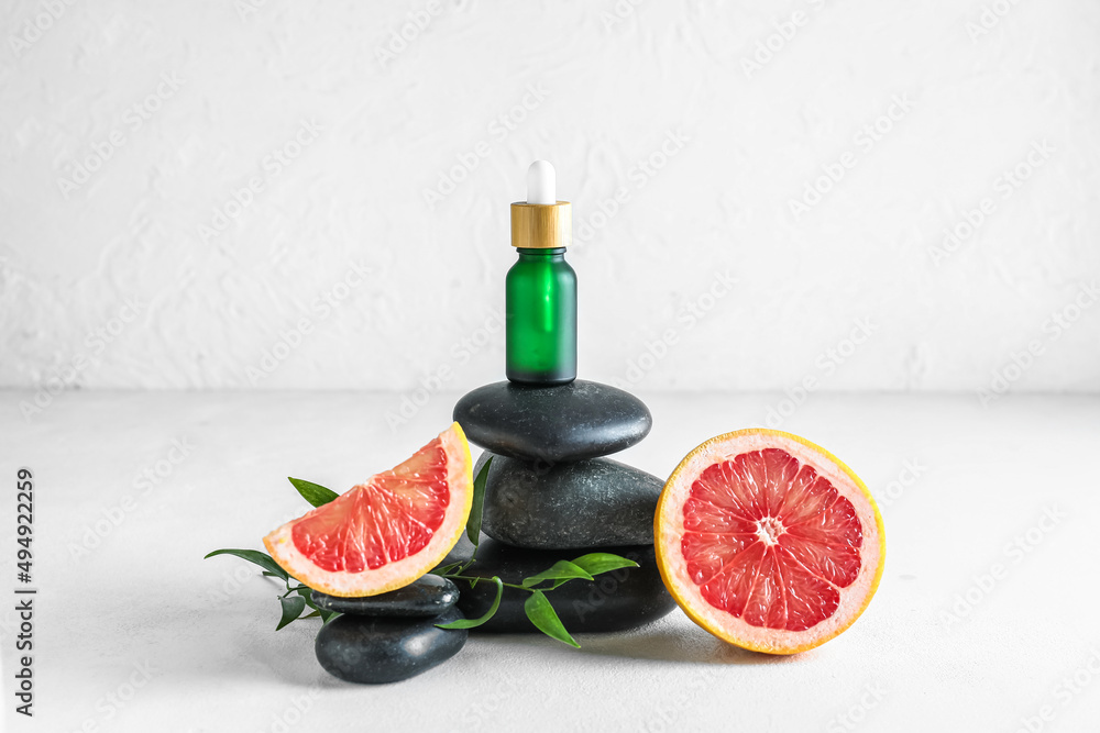 Composition with bottle of grapefruit essential oil and spa stones on light background