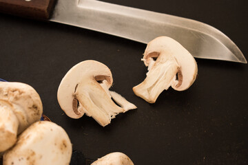 Sticker - Closeup shot of fresh sliced mushrooms with knife on a black surface